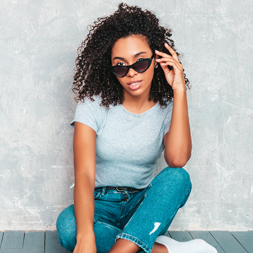 Woman sitting down, wearing fall clothes and wearing sunglasses.